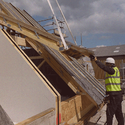man with hi-vis vest moving panelised roof into place on crane